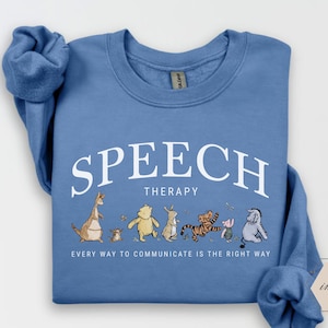 May include: A blue sweatshirt with the words "SPEECH THERAPY" in white arched text. Below, a line of cartoon characters, including Winnie the Pooh and Tigger, are featured. The text "EVERY WAY TO COMMUNICATE IS THE RIGHT WAY" is printed below the characters.