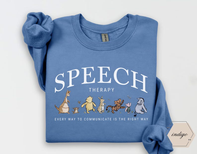 May include: A blue sweatshirt with the words "SPEECH THERAPY" in white arched text. Below, a line of cartoon characters, including Winnie the Pooh and Tigger, are featured. The text "EVERY WAY TO COMMUNICATE IS THE RIGHT WAY" is printed below the characters.