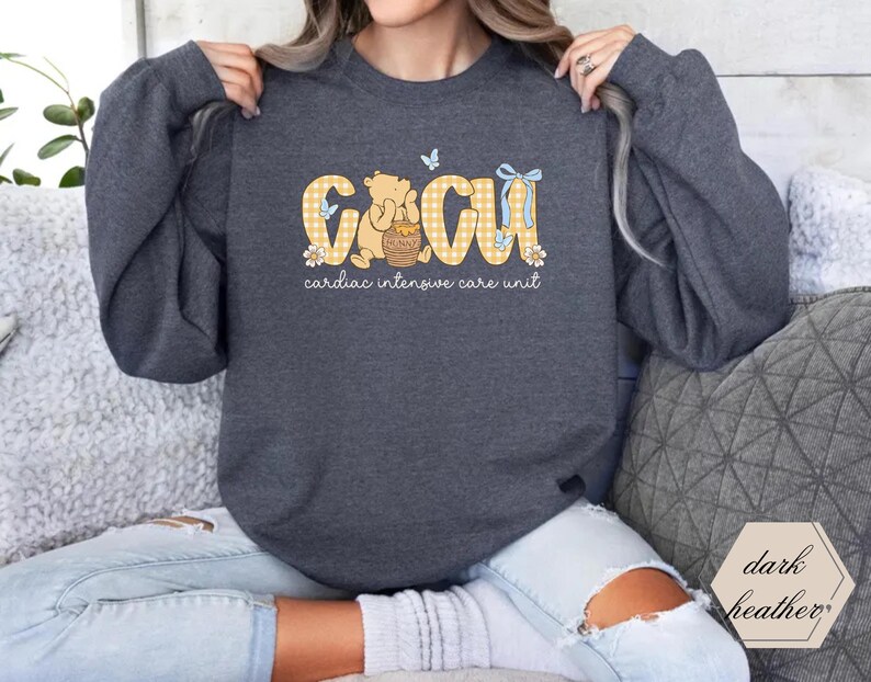 May include: Dark grey sweatshirt with a graphic reading "CCU cardiac intensive care unit". The design includes a Winnie the Pooh bear, honey pot, butterflies, and a yellow and white gingham pattern.
