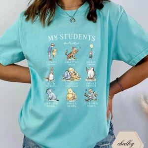 May include: A light blue t-shirt with the text "MY STUDENTS are" and illustrations of Winnie the Pooh characters. The shirt features phrases like "LOVED," "AMAZING," and "BRAVE."