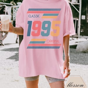 May include: A pink oversized t-shirt with a retro graphic design featuring the text "CLASSIC 1995 ORIGINAL" in colorful, layered stripes.