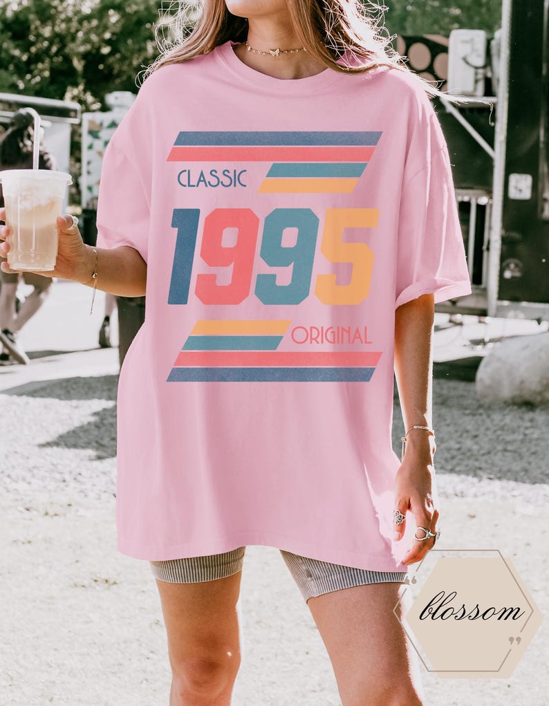 May include: A pink oversized t-shirt with a retro graphic design featuring the text "CLASSIC 1995 ORIGINAL" in colorful, layered stripes.