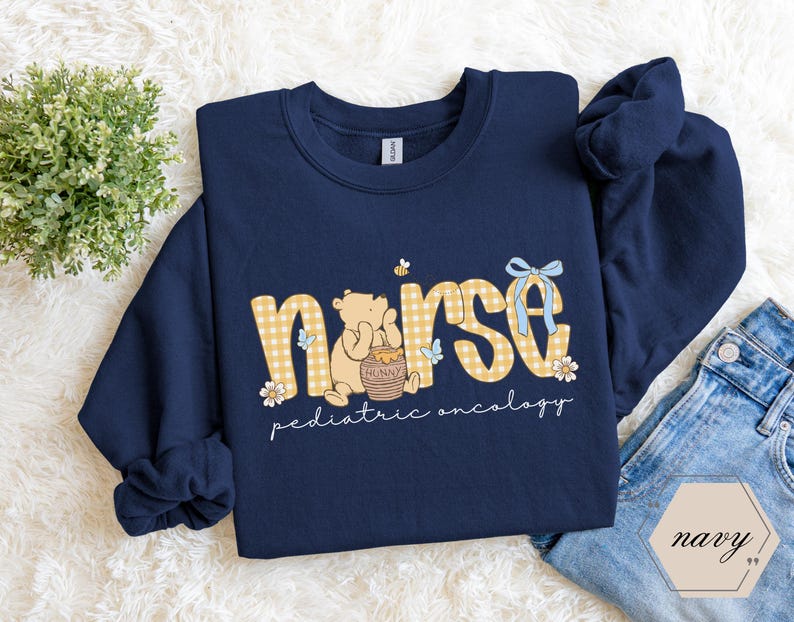 Peut inclure: Sweat-shirt bleu marine avec le mot "nurse" en imprim&eacute; vichy jaune, repr&eacute;sentant un ours de dessin anim&eacute; tenant un pot de miel. Le texte "pediatric oncology" est en dessous.