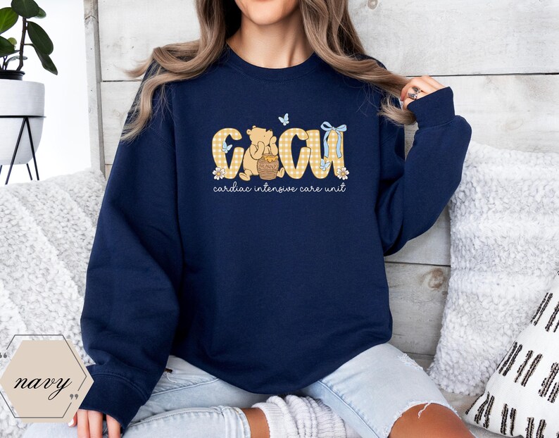 May include: Navy blue sweatshirt with the letters "CICU" in a yellow gingham pattern, featuring a cartoon bear holding a honey pot. The words "cardiac intensive care unit" are printed below the letters. A butterfly and bow accent the design.