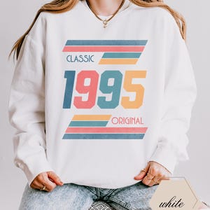 May include: White sweatshirt with a retro design featuring the year 1995 in colorful block letters and the words "Classic" and "Original" in black text.