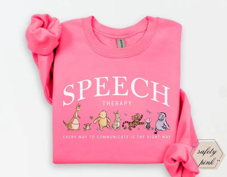 May include: A bright pink sweatshirt with the words "SPEECH THERAPY" in white arched text. Below the text are cartoon illustrations of Winnie the Pooh characters. The phrase "EVERY WAY TO COMMUNICATE IS THE RIGHT WAY" is printed below the illustrations.