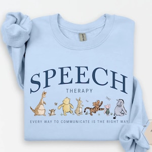 May include: Light blue sweatshirt with the words "SPEECH THERAPY" in navy blue arched across the top. Below the text is a line of cartoon characters. The phrase "EVERY WAY TO COMMUNICATE IS THE RIGHT WAY" is printed below the characters.