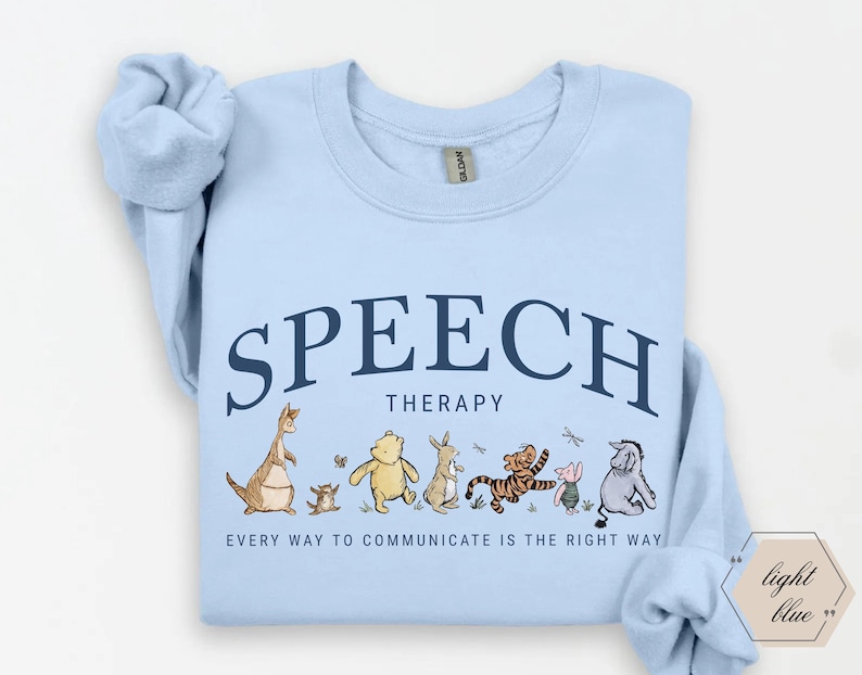 May include: Light blue sweatshirt with the words "SPEECH THERAPY" in navy blue arched across the top. Below the text is a line of cartoon characters. The phrase "EVERY WAY TO COMMUNICATE IS THE RIGHT WAY" is printed below the characters.