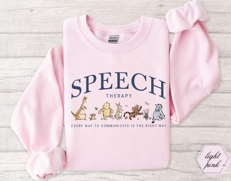 May include: Light pink sweatshirt with the words "SPEECH THERAPY" in navy blue arched across the top. Below the text are cartoon characters. The text "EVERY WAY TO COMMUNICATE IS THE RIGHT WAY" is printed below the characters.