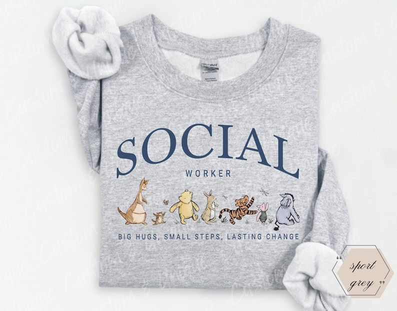 Pu&ograve; includere: Felpa grigio chiaro con la scritta blu navy "SOCIAL WORKER" ad arco nella parte superiore. Sotto il testo c'&egrave; una fila di personaggi dei cartoni animati. La parte inferiore della maglietta recita "BIG HUGS, SMALL STEPS, LASTING CHANGE."