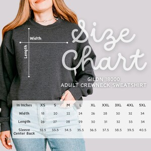 May include: A dark grey Gildan 18000 adult crewneck sweatshirt. The image includes a size chart with measurements in inches for width, length, and sleeve center back, ranging from XS to 5XL. The chart is labelled "Size Chart".