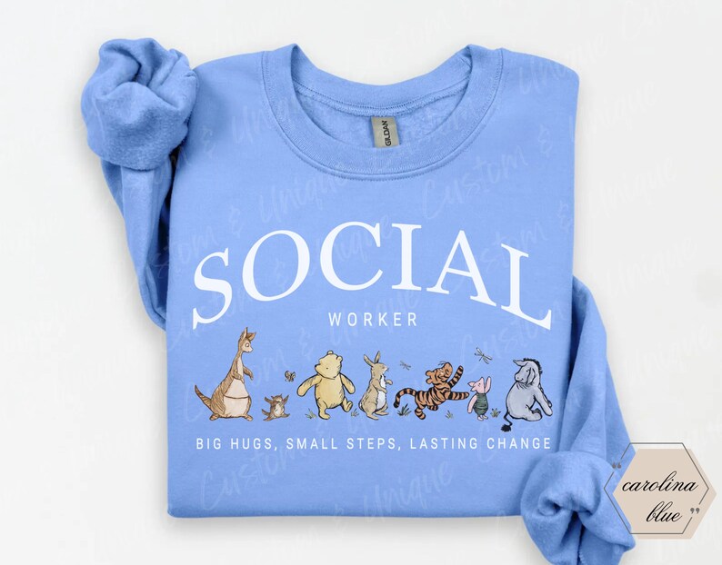 Pu&ograve; includere: Felpa blu Carolina con la scritta bianca "SOCIAL WORKER" e personaggi dei cartoni animati. Sotto, le parole "BIG HUGS, SMALL STEPS, LASTING CHANGE". La felpa ha un girocollo e maniche lunghe.