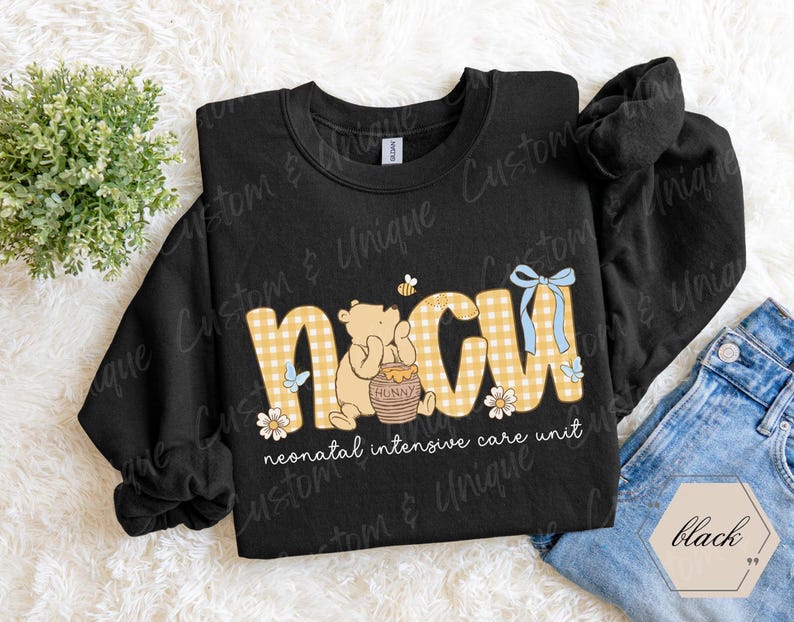 May include: Black sweatshirt with "NICU" in yellow gingham letters, featuring a cartoon bear with a honey pot, a bee, and floral accents. The text "neonatal intensive care unit" is below the letters. A blue bow is on the letter "U".