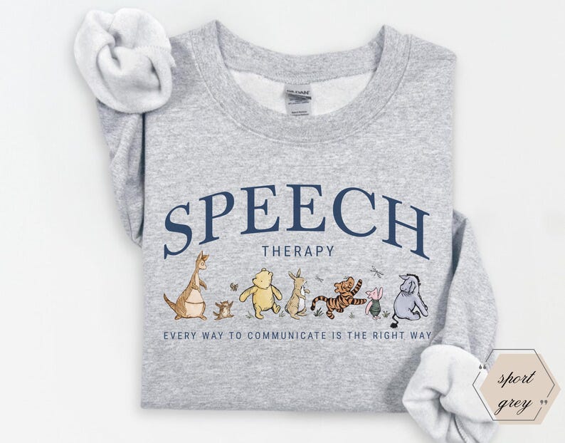 May include: A light gray sweatshirt with the words "SPEECH THERAPY" in navy blue arched text. Below, a line of cartoon characters. The text "EVERY WAY TO COMMUNICATE IS THE RIGHT WAY" is below the characters.