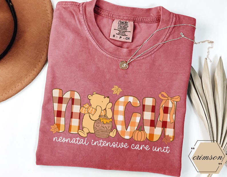 May include: A maroon Comfort Colors t-shirt with a graphic that reads "NICU" in plaid letters, featuring a cartoon bear with a honey pot and a pumpkin. The words "neonatal intensive care unit" are below the graphic.