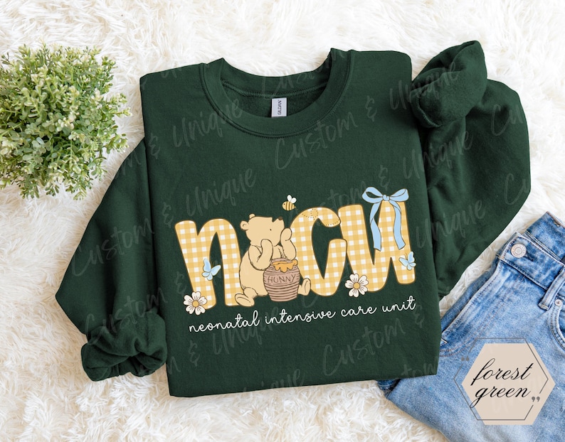 May include: Forest green sweatshirt with "NICU" in yellow gingham letters, Winnie the Pooh graphic, and text "neonatal intensive care unit." Features a blue bow and floral accents. A cozy, long-sleeved top.