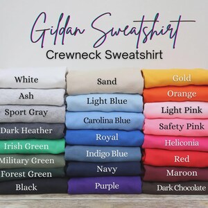 Pu&ograve; includere: Una pila di felpe girocollo Gildan in vari colori, tra cui bianco, cenere, grigio sport, grigio scuro e nero. Altri colori includono verde irlandese, verde militare, verde foresta, sabbia, azzurro e oro. L'immagine mostra anche arancione, rosa, rosso e marrone scuro.