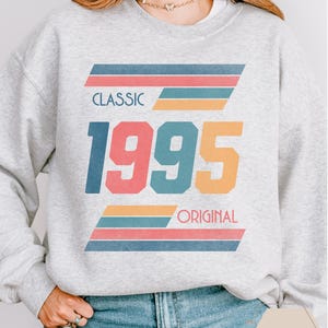 May include: A gray sweatshirt with a retro-style graphic design featuring the text "CLASSIC 1995 ORIGINAL" in colorful, bold letters with multi-colored stripes.
