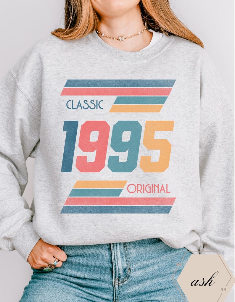 May include: A gray sweatshirt with a retro-style graphic design featuring the text "CLASSIC 1995 ORIGINAL" in colorful, bold letters with multi-colored stripes.