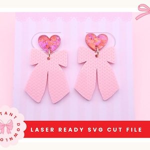 Könnte beinhalten: Ein Paar rosa Schleifenohrringe mit strukturierter Oberfläche. Jeder Ohrring hat einen herzförmigen Aufsatz mit einem bunten, glitzernden Design. Die Ohrringe werden auf einem rosa Hintergrund mit dem Text "LASER READY SVG CUT FILE" präsentiert.
