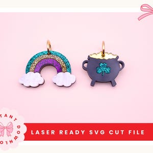 Può includere: Due ciondoli a tema San Patrizio. Uno è un arcobaleno con glitter turchese, oro e viola e nuvole bianche. L'altro è un pentolone d'oro nero con un trifoglio verde glitterato. Viene visualizzato il testo "LASER READY SVG CUT FILE".