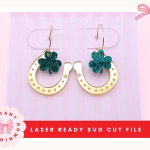 May include: Gold horseshoe earrings with a green glitter shamrock charm. The earrings are displayed on a white card with the text "LASER READY SVG CUT FILE" on a red banner. The background is pink.