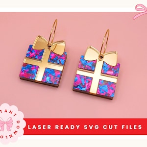 Puede incluir: Pendientes con forma de cajas de regalo con lazos dorados y detalles de cruz. Las cajas presentan un colorido patrón azul y rosa, suspendidas de aros dorados. El texto "LASER READY SVG CUT FILES" es visible en la parte inferior.