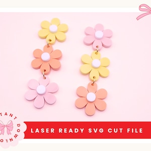 Puede incluir: Pendientes con forma de margarita en colores pastel. Cada pendiente presenta tres flores en amarillo, melocotón y rosa, con un centro blanco. Los pendientes están conectados por pequeños aros dorados. El texto "LASER READY SVG CUT FILE" es visible.