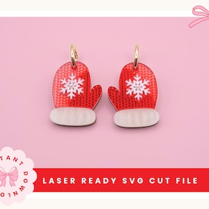 May include: A pair of red mitten-shaped charms featuring a white snowflake pattern and a white cuff at the base. Each charm includes a gold-toned metal jump ring at the top. The text LASER READY SVG CUT FILE is displayed at the bottom of the image.