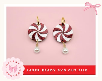 May include: A pair of candy-themed earrings. Each earring features a red and white swirled design with a gold hoop and a dangling white pearl. The earrings are set against a pink background. The text "LASER READY SVG CUT FILE" is visible.