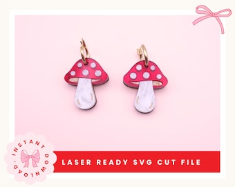 Puede incluir: Un par de pendientes con forma de seta, con sombreros rojos y puntos blancos. Los tallos de las setas son blancos con efecto nacarado. Los pendientes tienen aros dorados. El texto "LASER READY SVG CUT FILE" es visible.