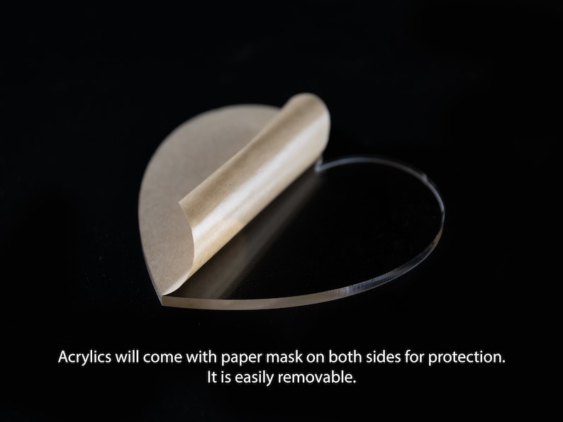 May include: A clear acrylic heart shape with a brown paper protective mask on one side. The mask is partially peeled back to reveal the clear acrylic.