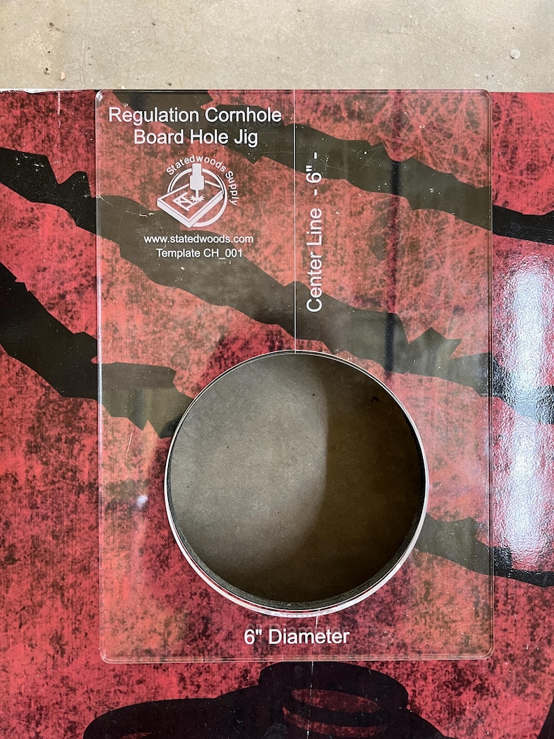 May include: A clear acrylic regulation cornhole board hole jig. The jig has a 6-inch diameter hole and is marked with a center line. Text on the jig includes "Regulation Cornhole Board Hole Jig" and "Statedwoods Supply".