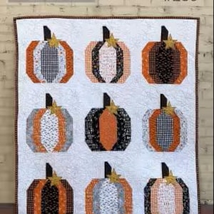 May include: A quilted wall hanging featuring nine geometric pumpkins in shades of orange, black, and white. Each pumpkin has a gold star stem and is set against a white background. The text "The Pumpkin Patch #250" is visible.