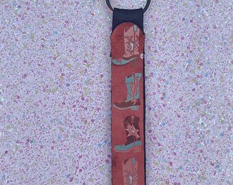 May include: A red, white, and blue patterned key chain with a black strap and a silver key ring. The pattern features a repeated design of cowboy boots.