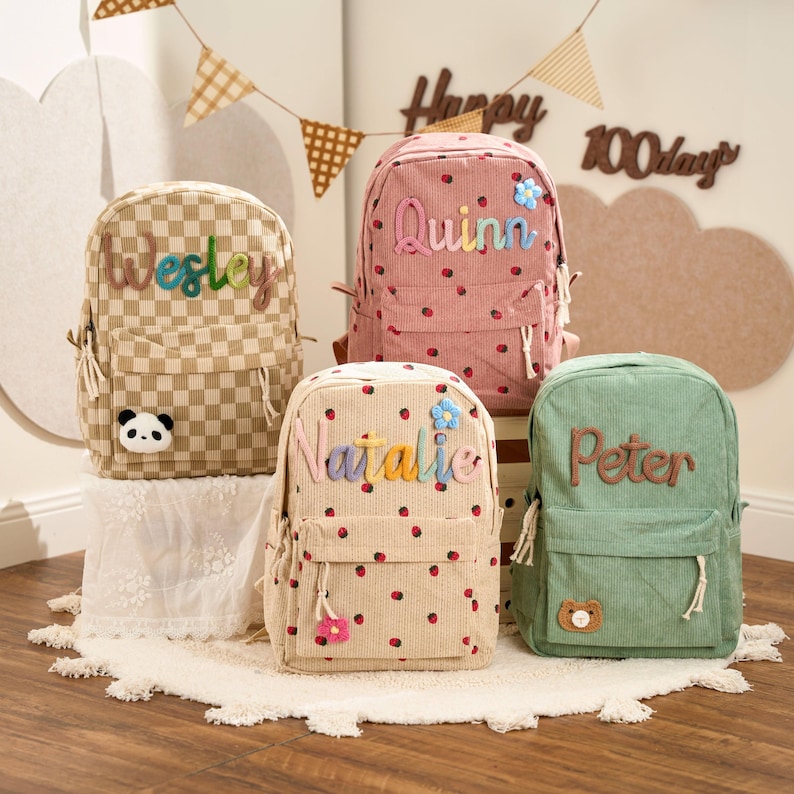 May include: Four corduroy backpacks in various colors: tan checkered, pink with red dots, tan with red dots, and green. Each backpack has a name embroidered on it: Wesley, Quinn, Natalie, and Peter. Decorative elements include a panda, flowers, and a bear.