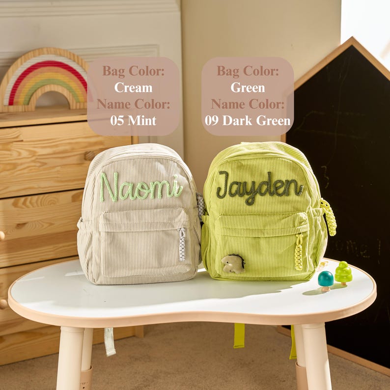 May include: Two corduroy backpacks featuring front pockets and zippers. The cream backpack displays the name Naomi in mint green embroidery. The green backpack displays the name Jayden in dark green embroidery and includes a small dinosaur charm.