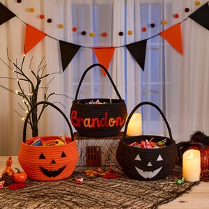 May include: Three round woven baskets for Halloween. One orange basket features a black jack-o'-lantern face, one black basket features a white jack-o'-lantern face, and one black basket features the name Brandon in orange and red felt letters.