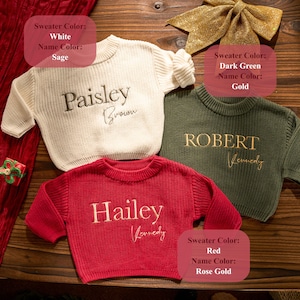 May include: Three personalised sweaters in white, dark green, and red. Each sweater has a name embroidered in a contrasting colour. The white sweater has "Paisley Brown" in sage. The dark green sweater has "ROBERT Kennedy" in gold. The red sweater has "Hailey Kennedy" in rose gold.