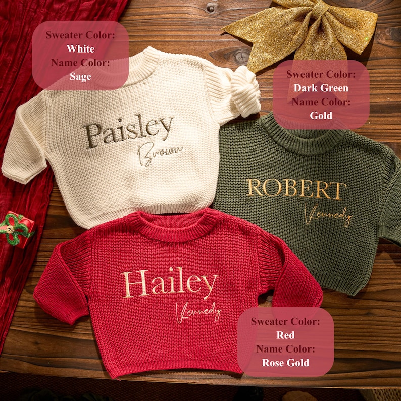 May include: Three personalised sweaters in white, dark green, and red. Each sweater has a name embroidered in a contrasting colour. The white sweater has "Paisley Brown" in sage. The dark green sweater has "ROBERT Kennedy" in gold. The red sweater has "Hailey Kennedy" in rose gold.