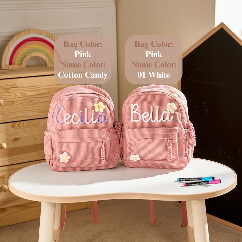 May include: Two pink corduroy backpacks featuring embroidered names and small flower appliqu&eacute;s. The left bag displays the name Cecilia in light purple, and the right bag displays the name Bella in white. Text labels indicate bag and name colours.
