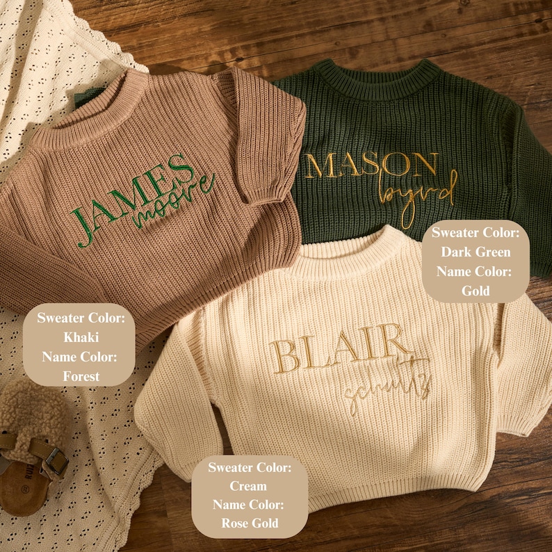 May include: Three personalised sweaters in khaki, dark green, and cream. Each sweater has a name embroidered in a contrasting colour: green, gold, and rose gold. The sweaters are displayed on a wooden surface.