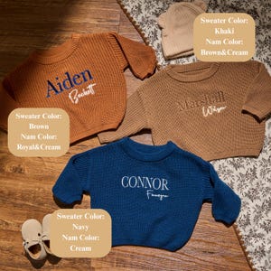 May include: Three personalised children's sweaters in brown, khaki, and navy blue. Each sweater has a name embroidered in a contrasting colour. A matching beanie and a pair of shoes are also visible. The sweaters are knitted.