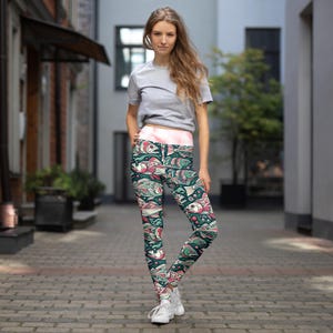 Peut inclure: Une femme porte un legging noir avec un motif de poissons colorés. Le legging a une ceinture rose et est fait d'un matériau extensible. La femme est debout dans une rue de la ville.
