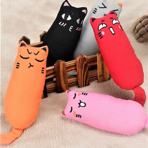 以下が含まれることがあります： オレンジ、黒、グレー、赤、ピンクなど、さまざまな色の猫の形をしたぬいぐるみが5つあります。おもちゃは刺繍された顔と尻尾をしています。