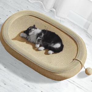 Könnte beinhalten: Ein ovaler Kratzbaum für Katzen aus Wellpappe. Eine schwarz-weiße Katze liegt auf dem Kratzbaum. Eine kleine, gewebte Kugel ist mit einer Schnur an der Seite befestigt.