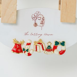 May include: A set of six Christmas-themed earrings featuring a candy cane, a bell, a gift box, a Christmas tree, and a wreath. The earrings are gold-toned with red, green, and white enamel.