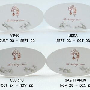 May include: Four pairs of silver stud earrings, each with a different zodiac sign design, are displayed on white oval cards. The cards include the zodiac signs Virgo, Libra, Scorpio, and Sagittarius, along with their corresponding dates. The text "The Earring Haven" is also visible.
