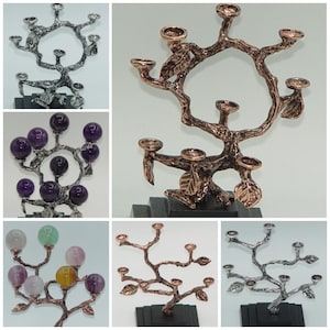 May include: A collection of decorative candle holders in various styles. The candle holders are made of metal and feature a tree branch design. Some have gemstone accents, while others have a metallic finish. Each is mounted on a black base.