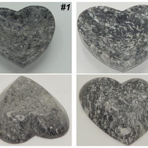 May include: Four heart-shaped decorative bowls. The bowls are made of gray stone with white veining. The bowls are in different orientations, showing the front, back, and side views. The bowls are on a white background.